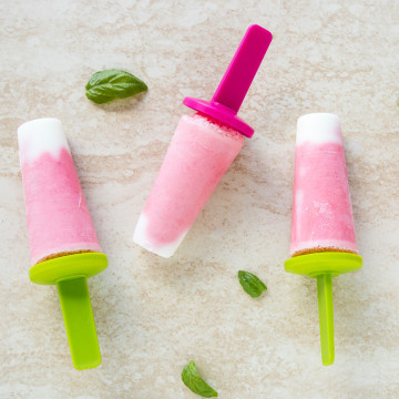 Three pink popsicles on a counter.