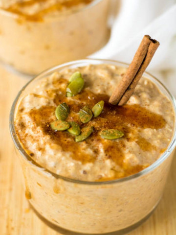Oatmeal in a cup with pumpkin seeds and a cinnamon stick on top.