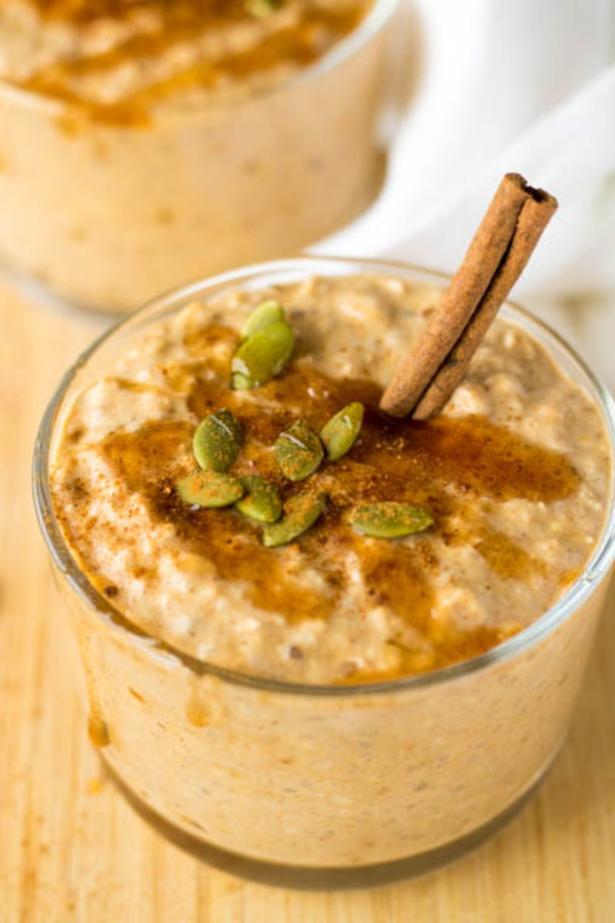 Oatmeal in a cup with pumpkin seeds and a cinnamon stick on top.