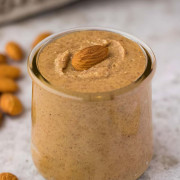 Almond butter in a small jar with whole almonds on the surface beside it.
