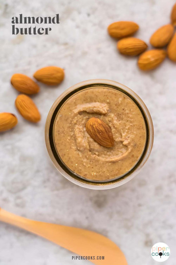 Almond butter in a small jar with whole almonds on the surface beside it.