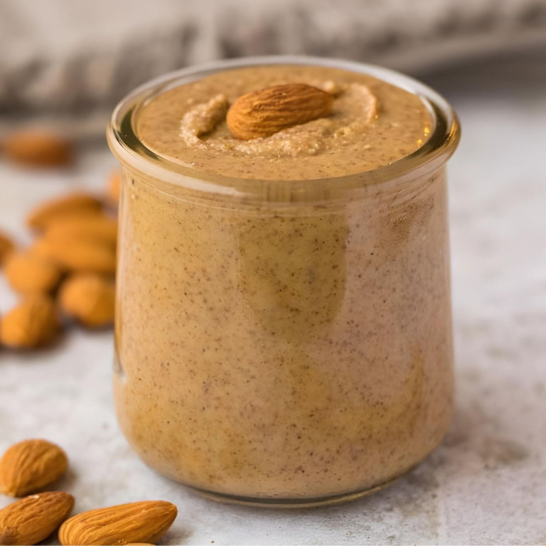 Almond butter in a small jar with whole almonds on the surface beside it.