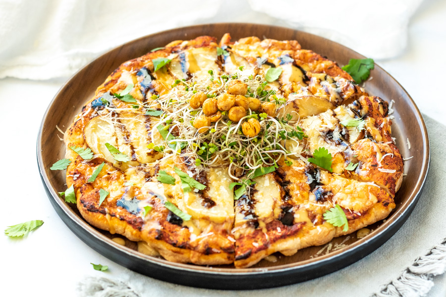 A potato pizza topped with a balsamic glaze, chickpeas, and microgreens.