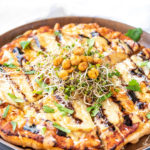 A potato pizza topped with a balsamic glaze, chickpeas, and microgreens.