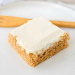 A square slice of a sheet cake with cream cheese frosting.