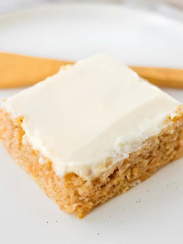 A square slice of a sheet cake with cream cheese frosting.