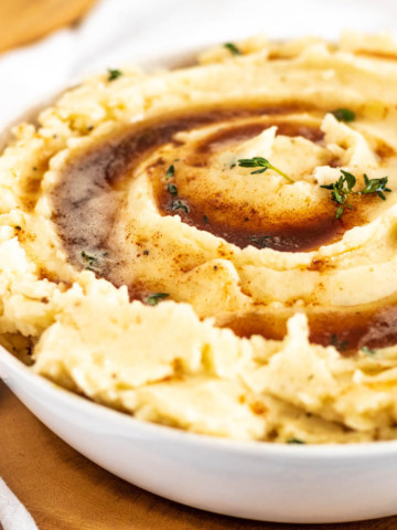 Mashed potatoes in a bowl topped with browned butter and thyme.