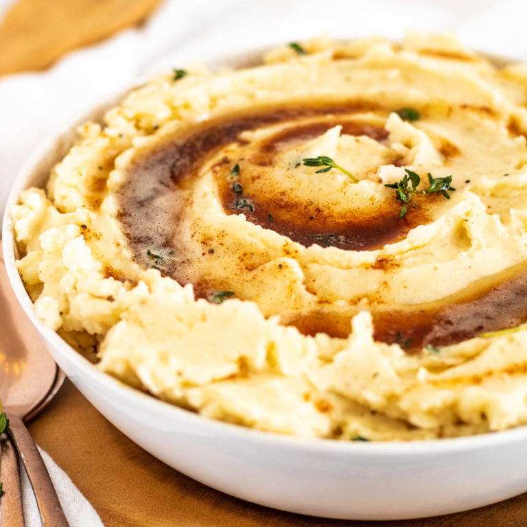 Mashed potatoes in a bowl topped with browned butter and thyme.