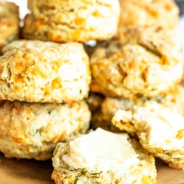 a pile of biscuits on a wood board with one open and buttered