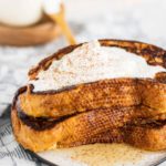 eggnog french toast on a plate with syrup, whipped cream and sprinkle of nutmeg