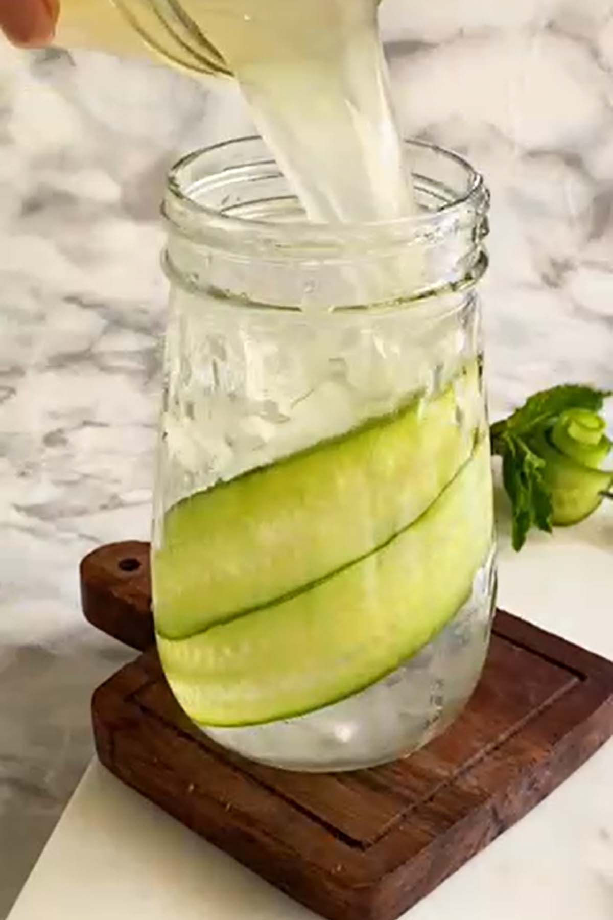 Lemonade is poured into a glass with cucumber ribbons along the side.