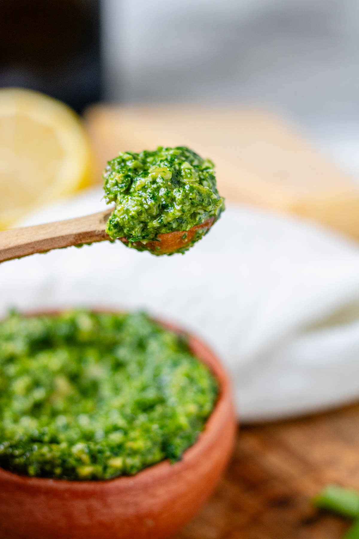 Vibrant green pesto in an orange clay bowl and on a wooden spoon.
