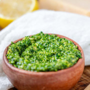 Vibrant green pesto in an orange clay bowl with a text title for Pinterest.