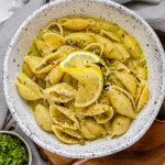 Pasta shells in a yellow sauce with pepper, grated cheese, and a lemon slice on top.