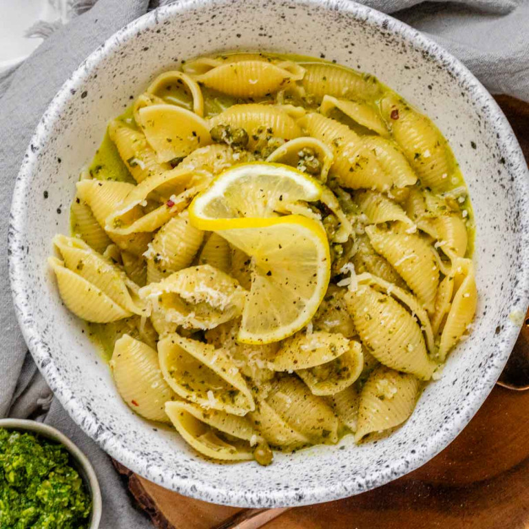 Pasta shells in a yellow sauce with pepper, grated cheese, and a lemon slice on top.
