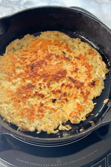 A potato rosti cooks in a cast iron pan with a crispy top.