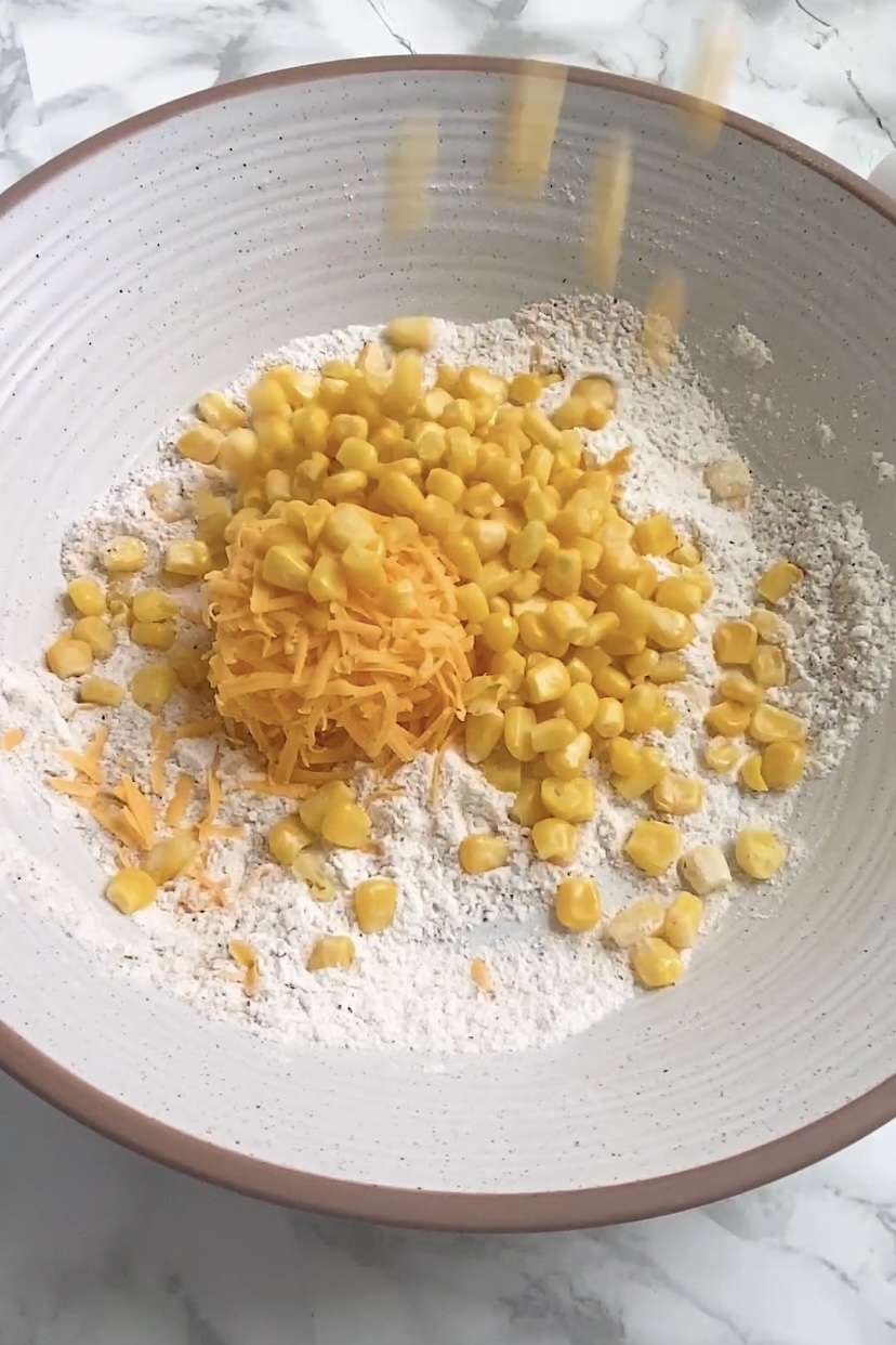 Corn is dropped into a bowl with flour and cheese in it.