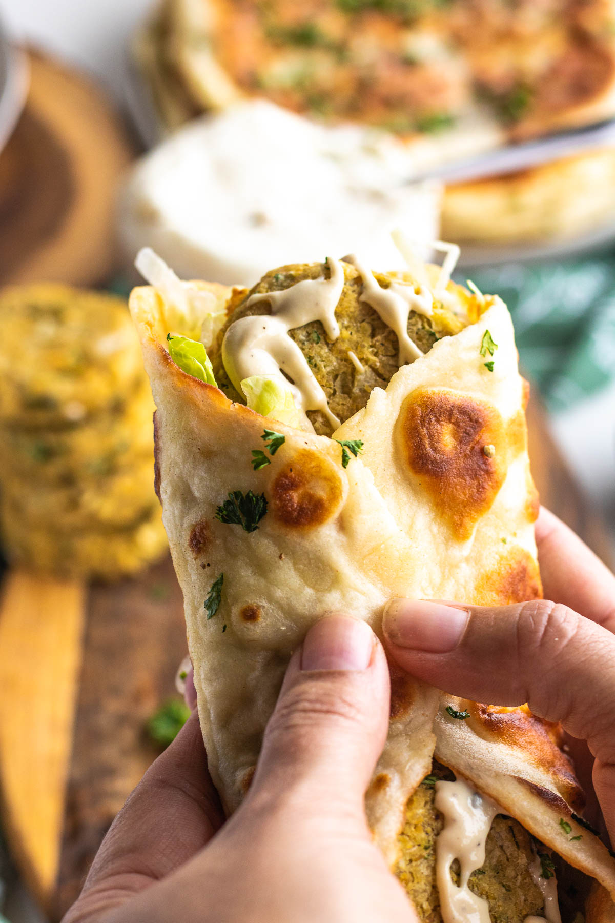 hands holding a flatbread wrapped with chickpea patties inside