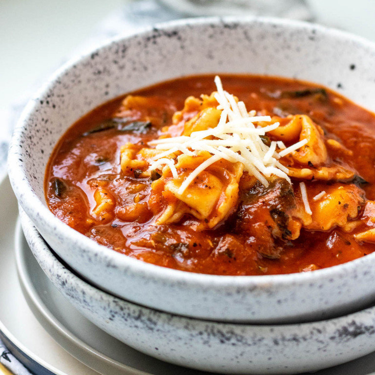 tomato tortellini soup in a white speckled bowl