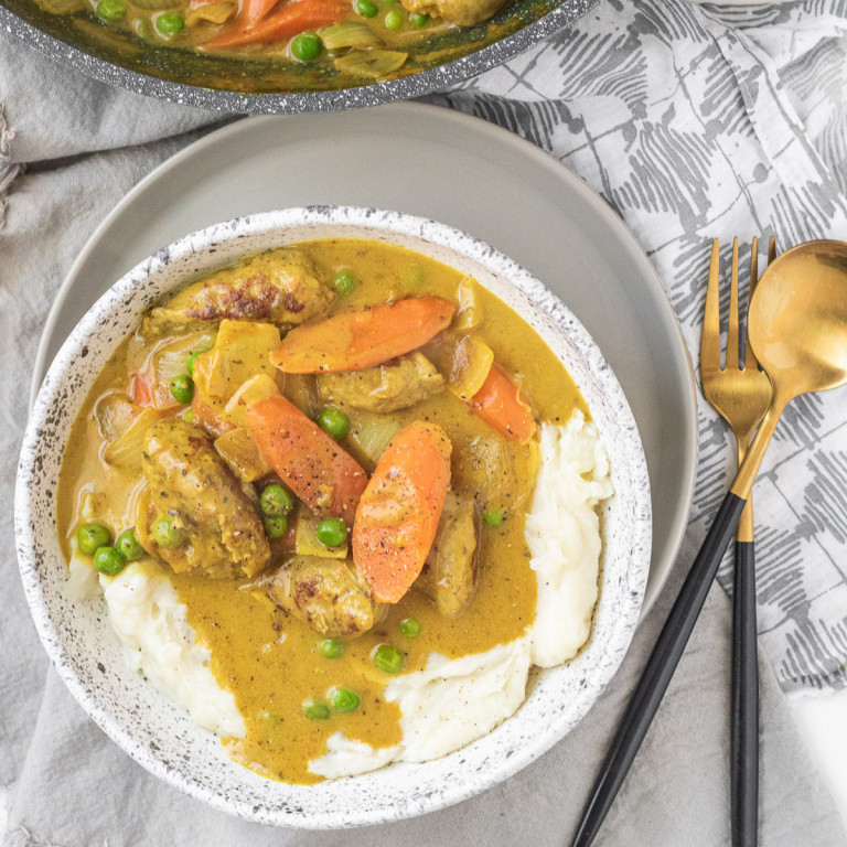 Sausage curry in a bowl, on top of mashed potatoes.
