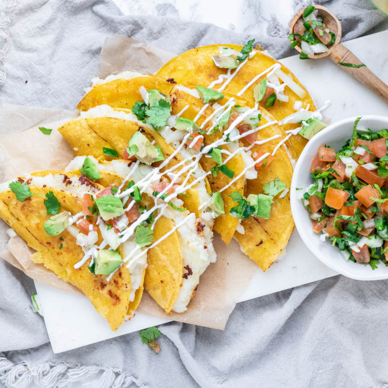 potato tacos on a platter with avocado and salsa on top