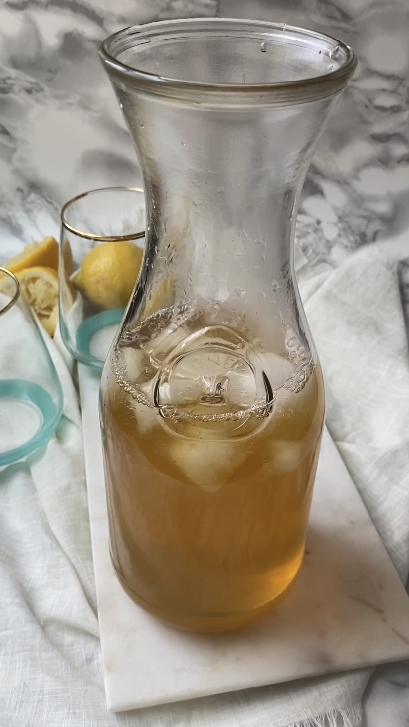 Adding ice to green tea lemonade in a pitcher.