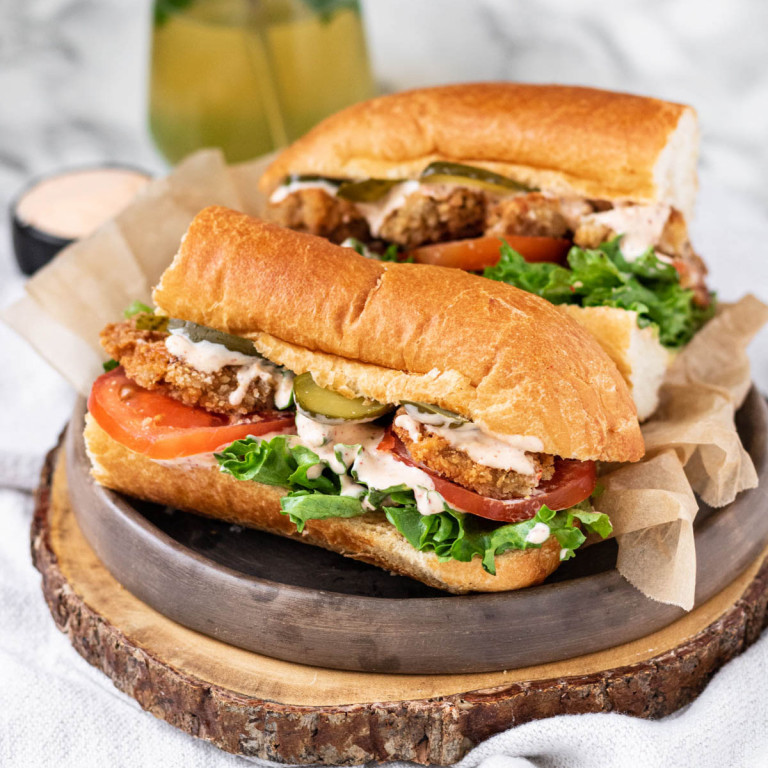 A sandwich filled with mushrooms, lettuce and tomato, on a wood platter.