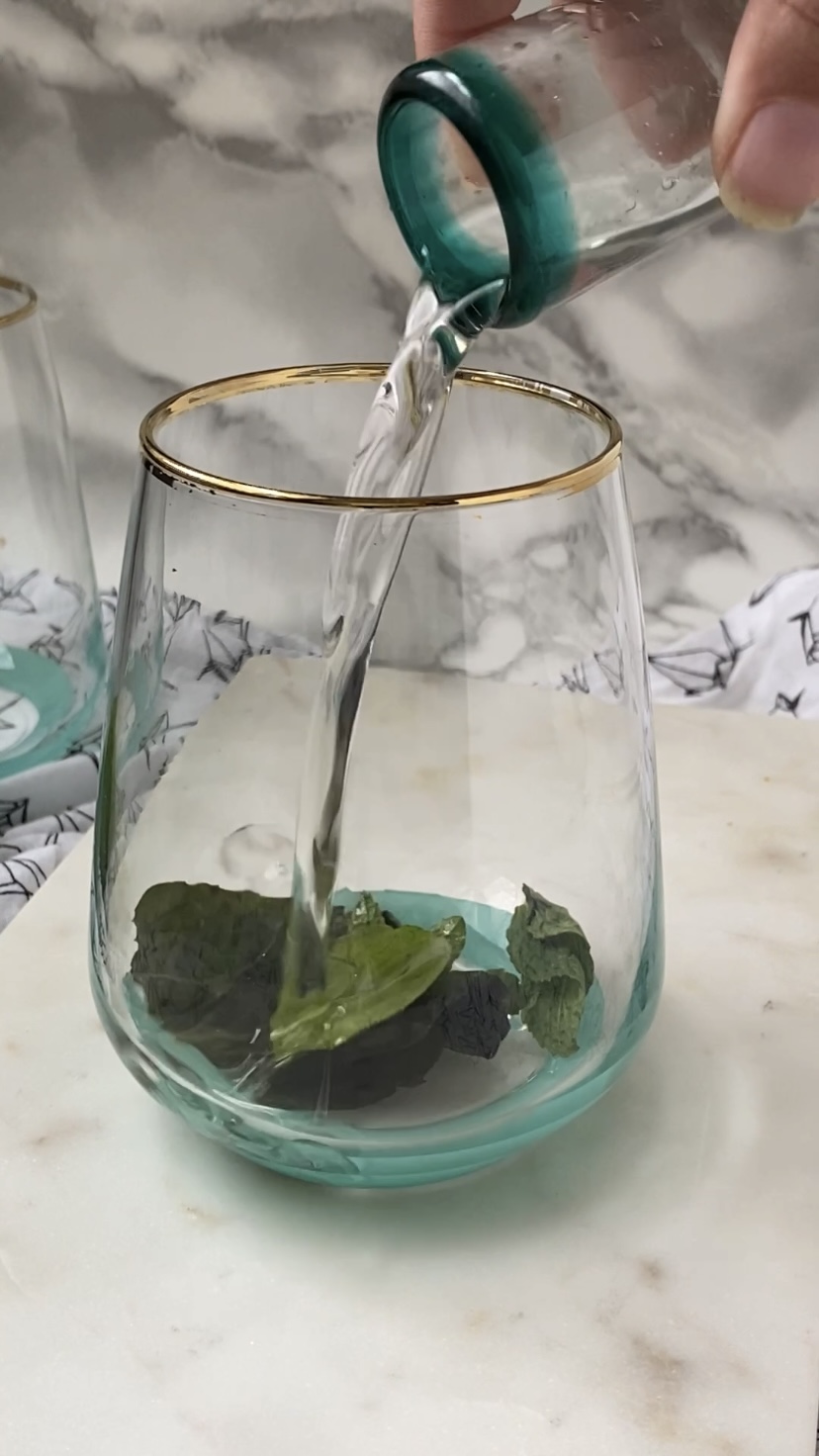Adding simple syrup to a cocktail glass of mint leaves.