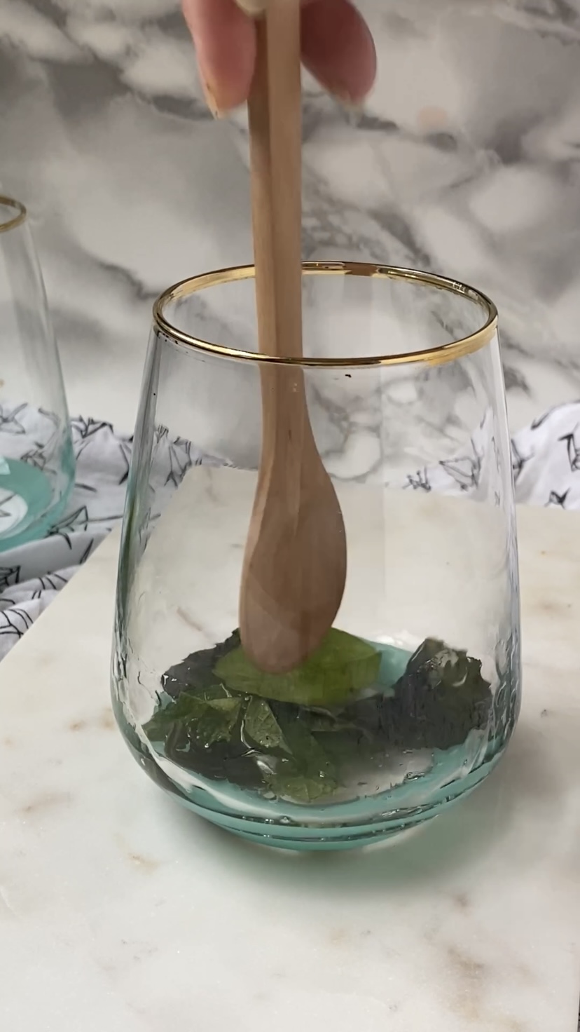 Muddling leaves and simple syrup with a wooden spoon.
