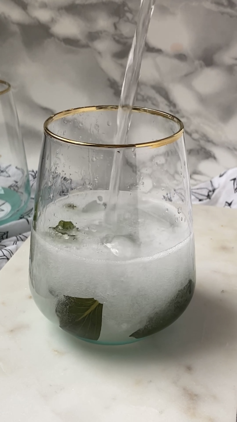 Adding sparkling water to a cocktail glass.