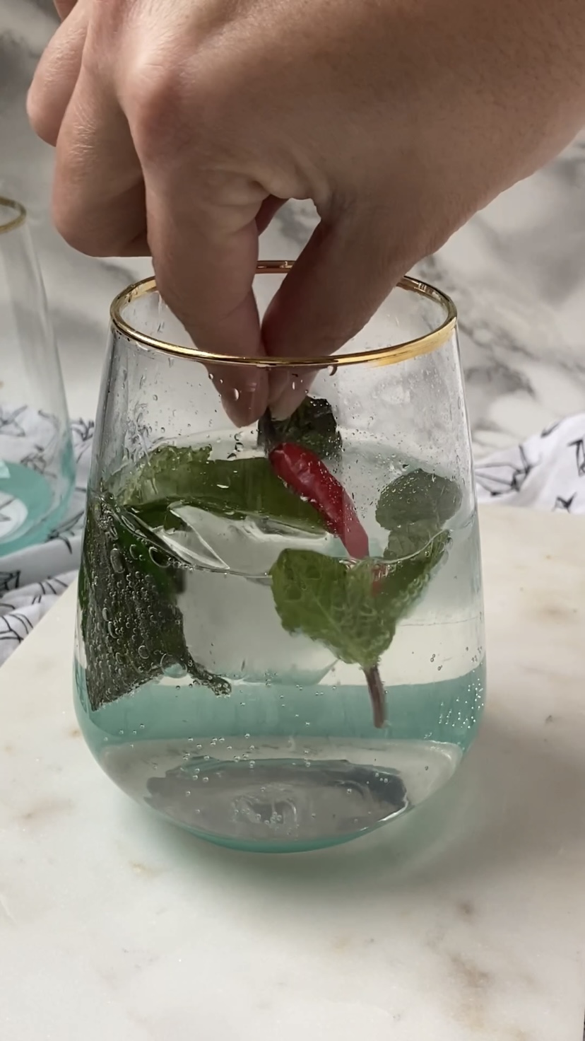 Adding a red Thai chili to a cocktail glass.