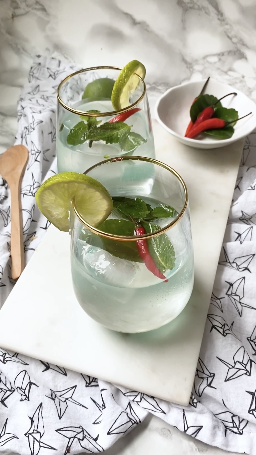Two cocktails garnished with Thai leaves and chilies on a marble background.