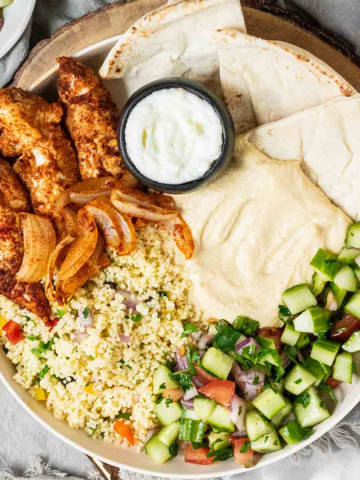 A chicken shawarma plate with chicken, pita, sauces, couscous and cucumber salad.