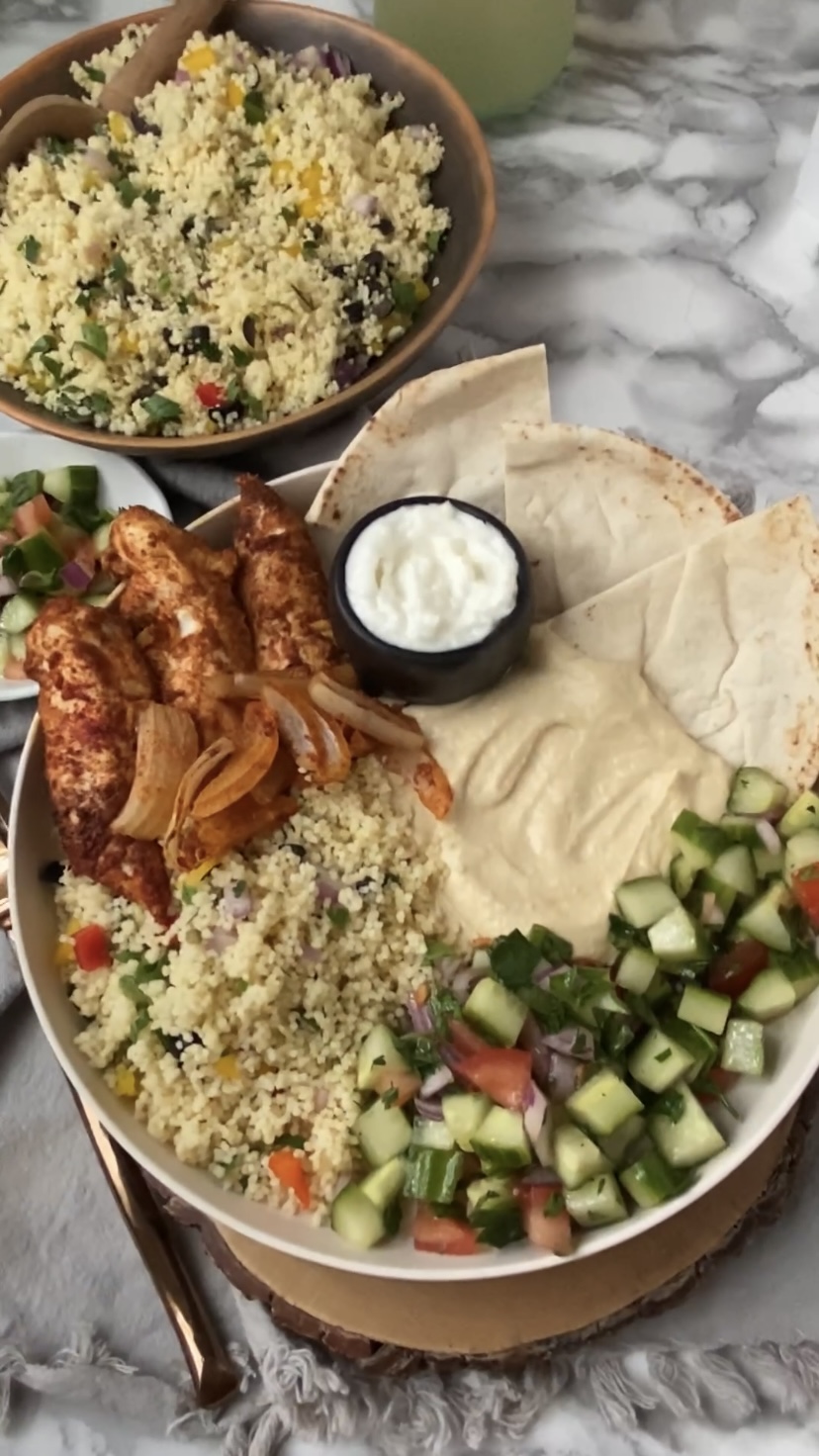 A chicken shawarma plate with chicken, pita, sauces, couscous and cucumber salad.