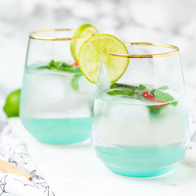 Two cocktails garnished with Thai leaves and chilies on a marble background.