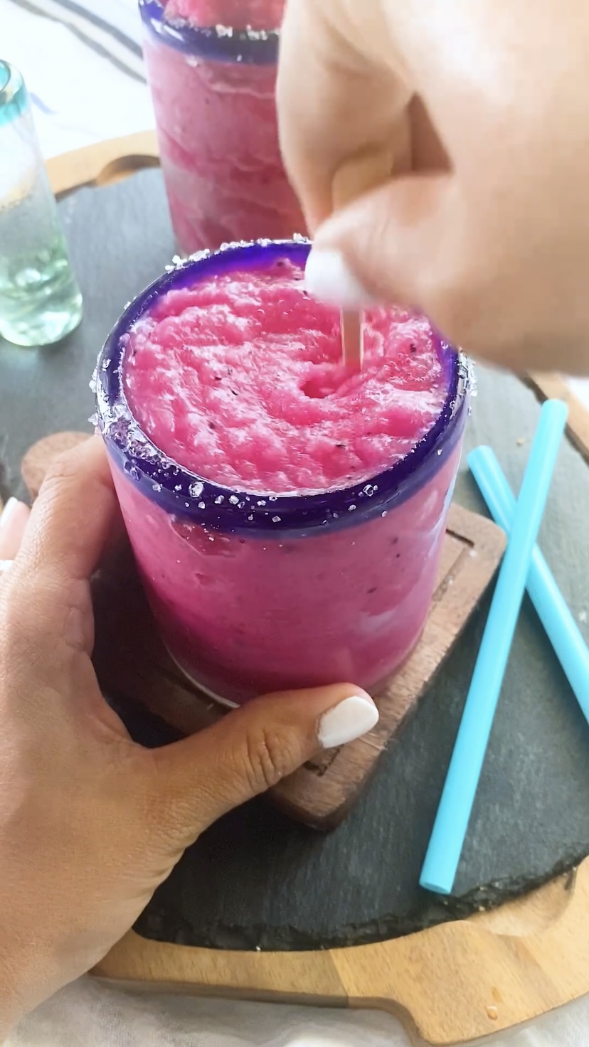 Stirring a bright pink frozen margarita in a blue-rimmed glass.