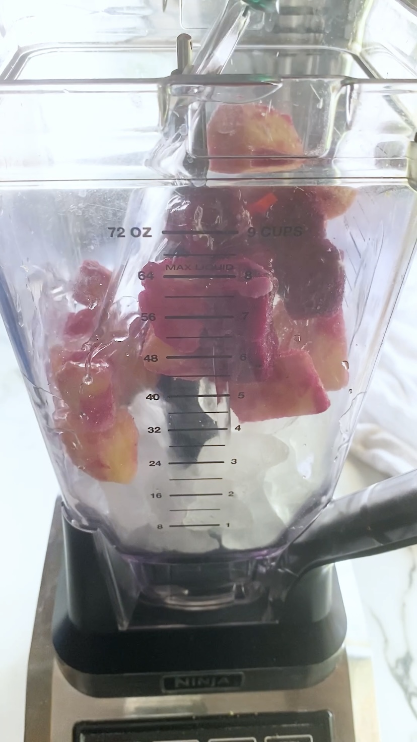 Adding liquid to a blender with frozen fruit and ice it.