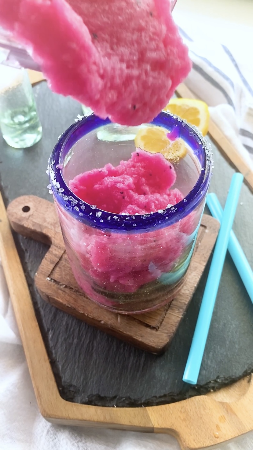 Pouring a bright pink frozen margarita into a blue-rimmed glass.