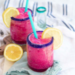 A bright pink blended margarita in a blue-rimmed glass with a blue straw and lemon garnish.