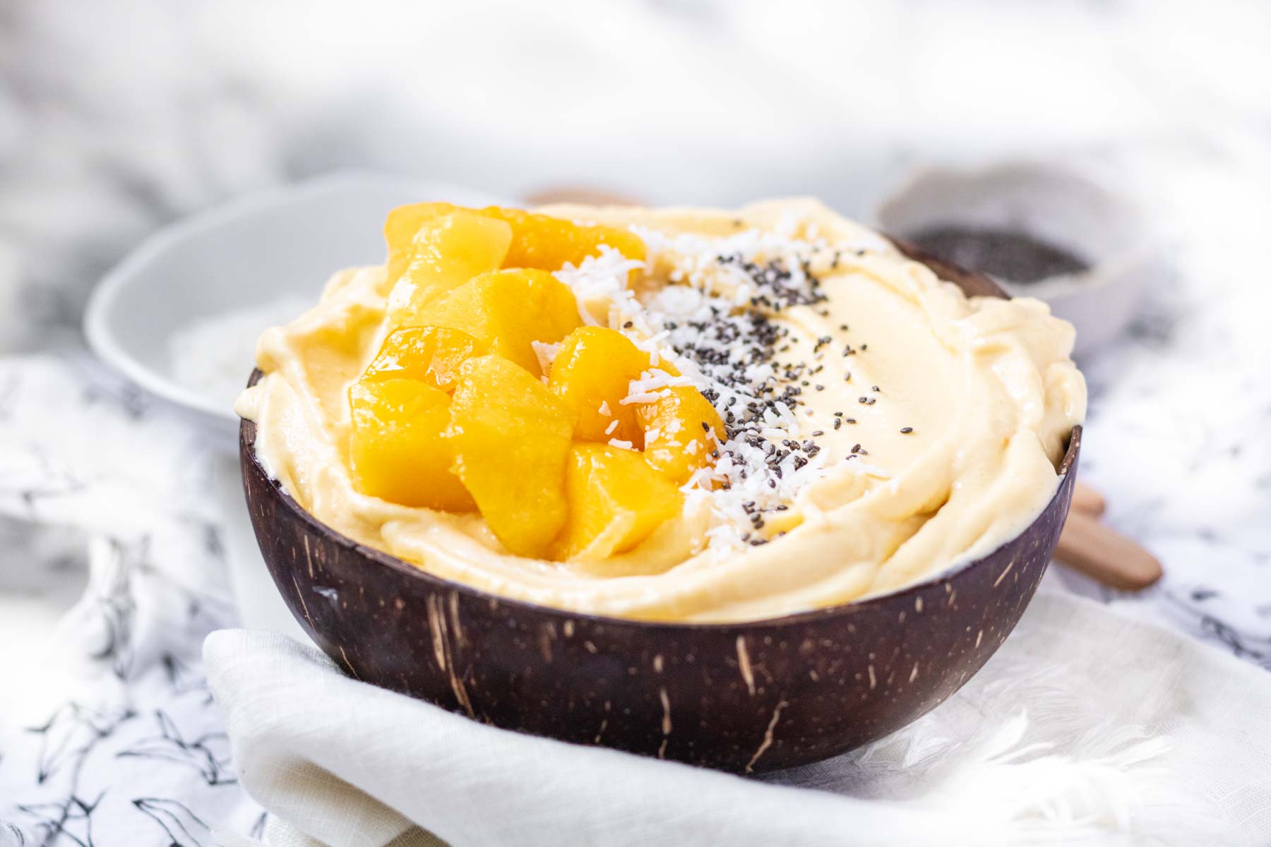 A mango smoothie bowl in a coconut bowl with mango chunks on top.