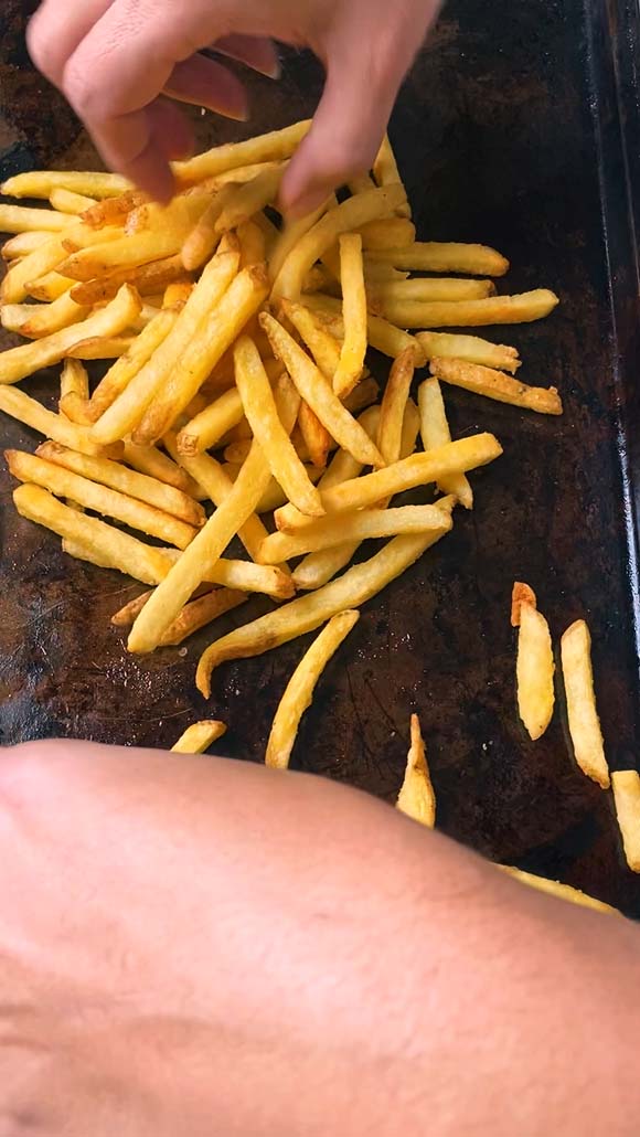 Pushing fries on a baking sheet into a pile.