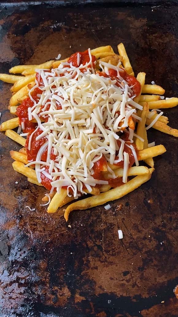 Shredded mozzarella cheese and pizza sauce on a pile of fries.