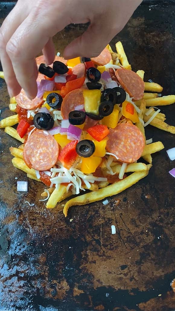 Add black onion to a pile of fries with pepperoni, pizza sauce, mozzarella, bell pepper and red onion on them.