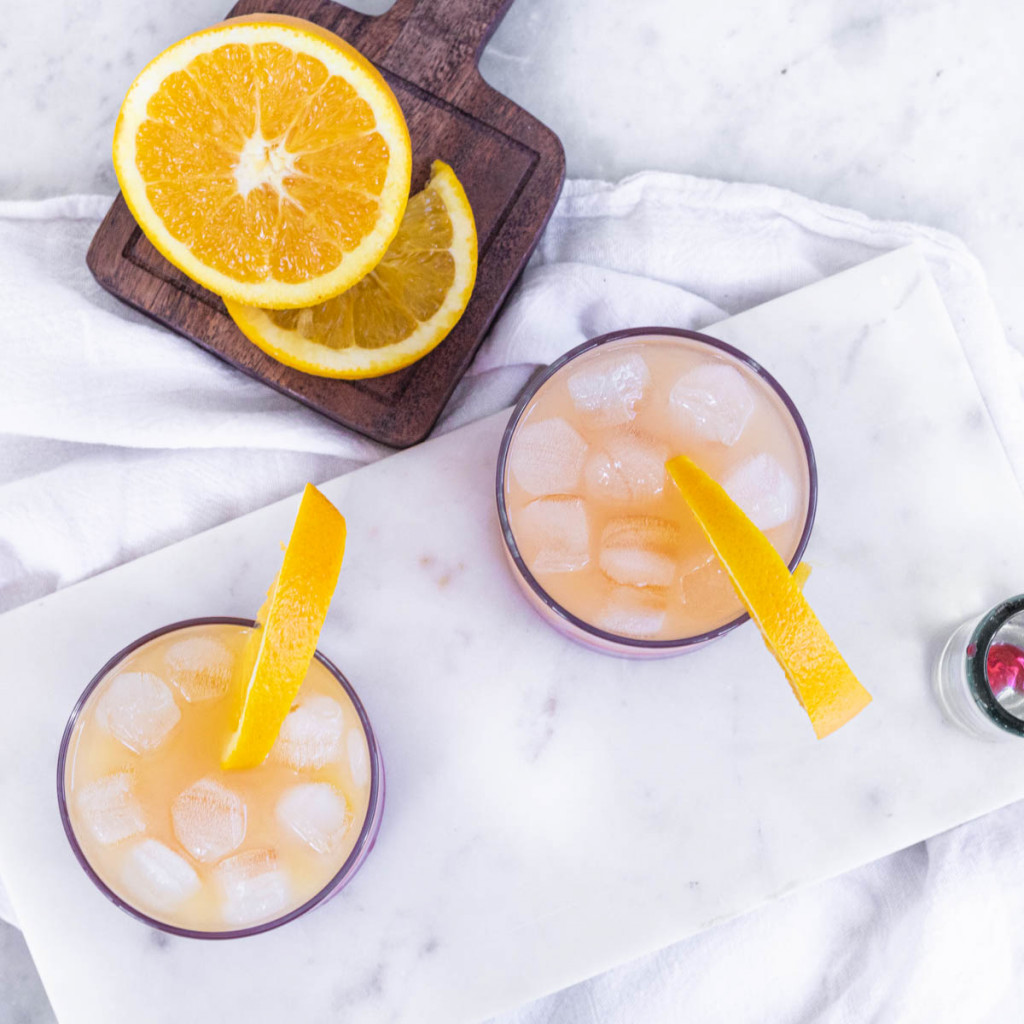 A red and orange cocktail in a glass, garnished with an orange slice.