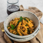 Curly pasta noodles with orange hummus sauce in a bowl.