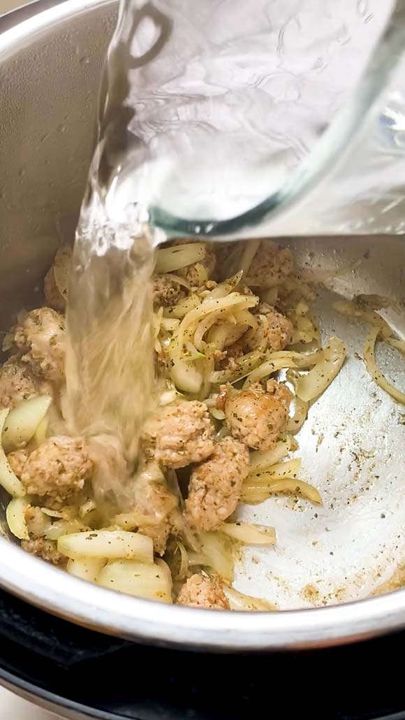 Adding water to onions and sausage in an Instant Pot.