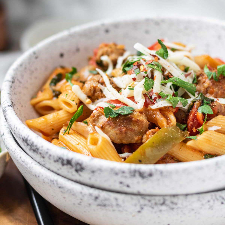 Pasta with sausages and spinach, in a bowl with shredded cheese and parsley on top.