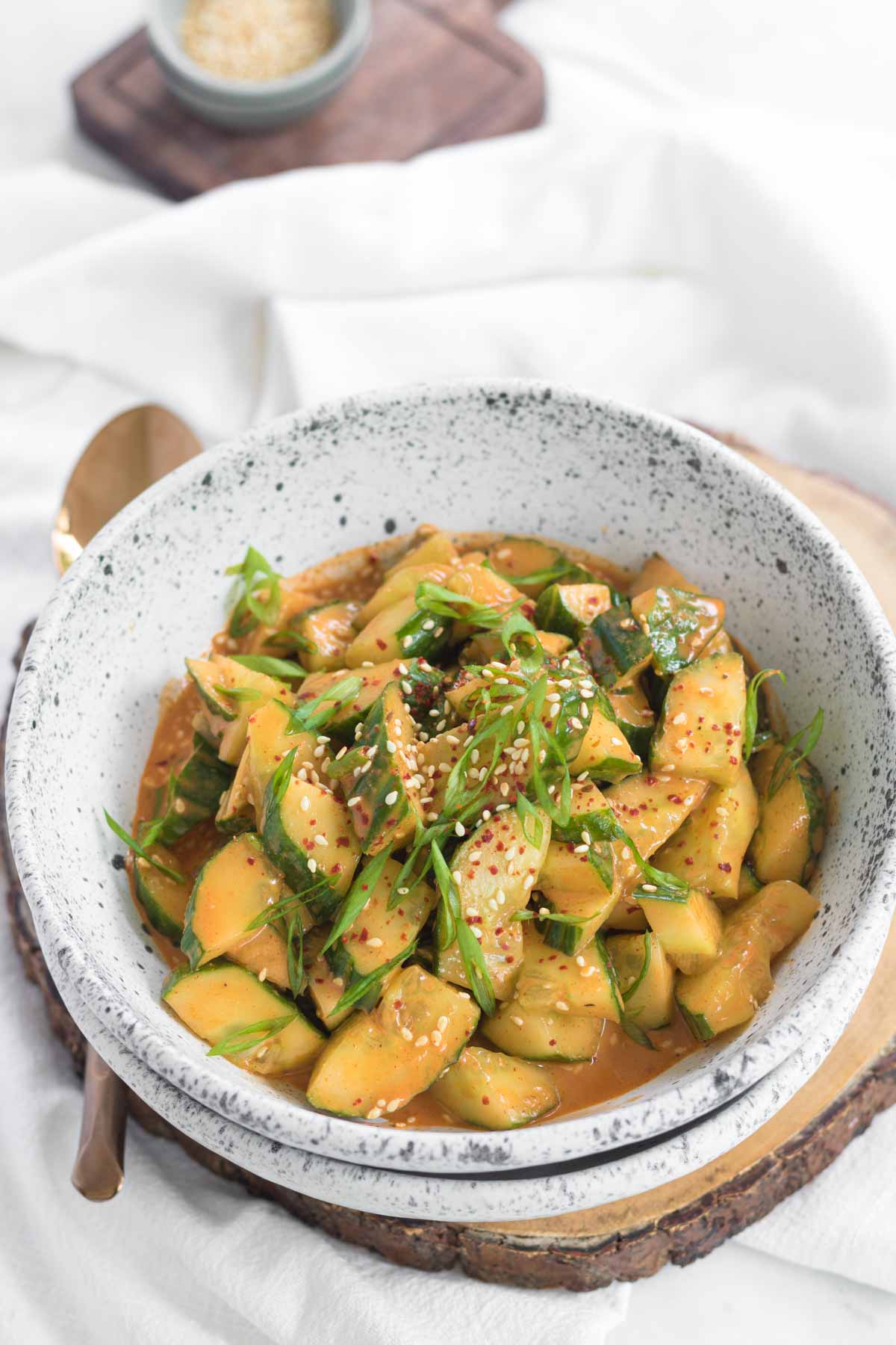 A bowl of smashed cucumbers in an orange sauce, garnished with sliced green onions.
