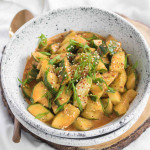 A bowl of smashed cucumbers in an orange sauce, garnished with sliced green onions.