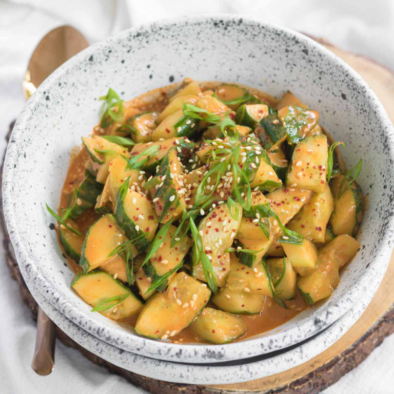A bowl of smashed cucumbers in an orange sauce, garnished with sliced green onions.